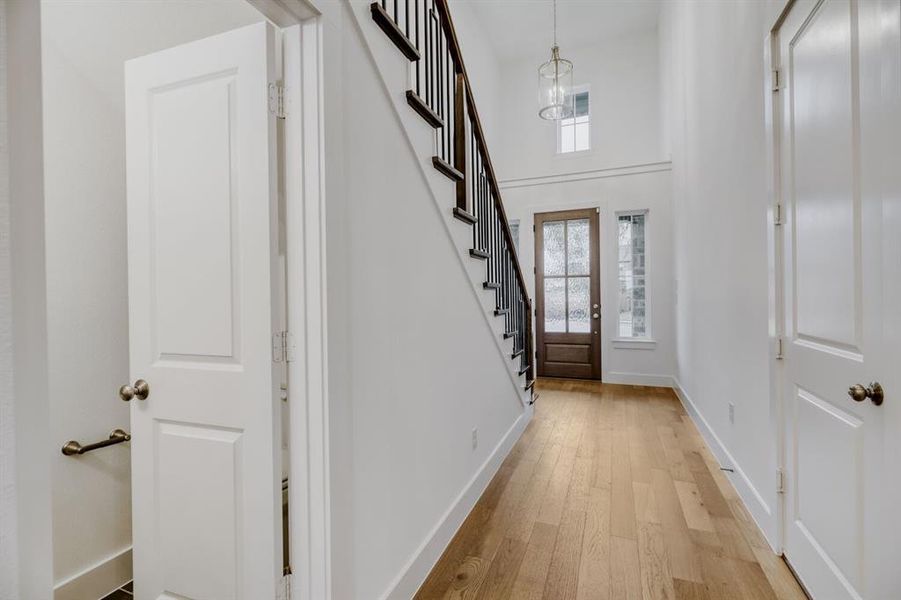 Entryway featuring wood-finish flooring, a dark wood entry door with frosted glass, and a two-story ceiling with a contemporary pendant light fixture