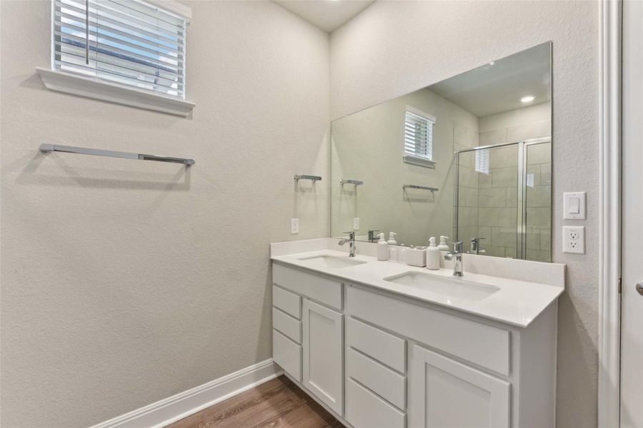 Bathroom featuring double vanity, a shower stall, a textured wall, and wood finished floors Bathroom featuring double vanity, a shower stall, a textured wall, and wood finished floors