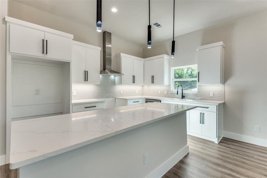 Kitchen with light hardwood / wood-style flooring, decorative light fixtures, wall chimney exhaust hood, white cabinets, and sink