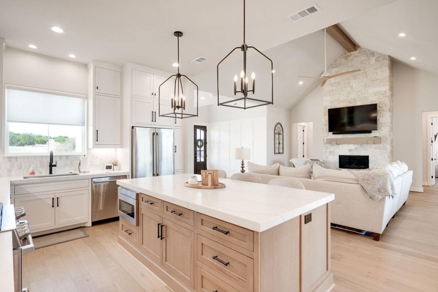 Kitchen featuring high end appliances, light wood finished floors, a kitchen island, open floor plan, and a stone fireplace