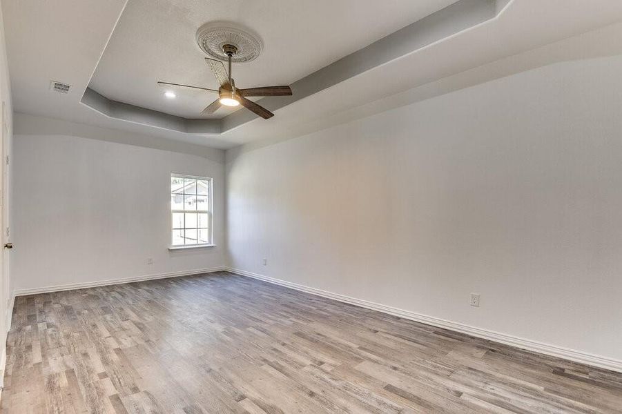 Empty room with ceiling fan, light wood-type flooring, and a raised ceiling