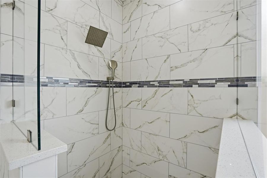 Shower enclosure featuring white marble-look tile walls with a mosaic accent band, a built-in shower bench with a light-toned countertop, a handheld shower fixture, and a rainfall showerhead