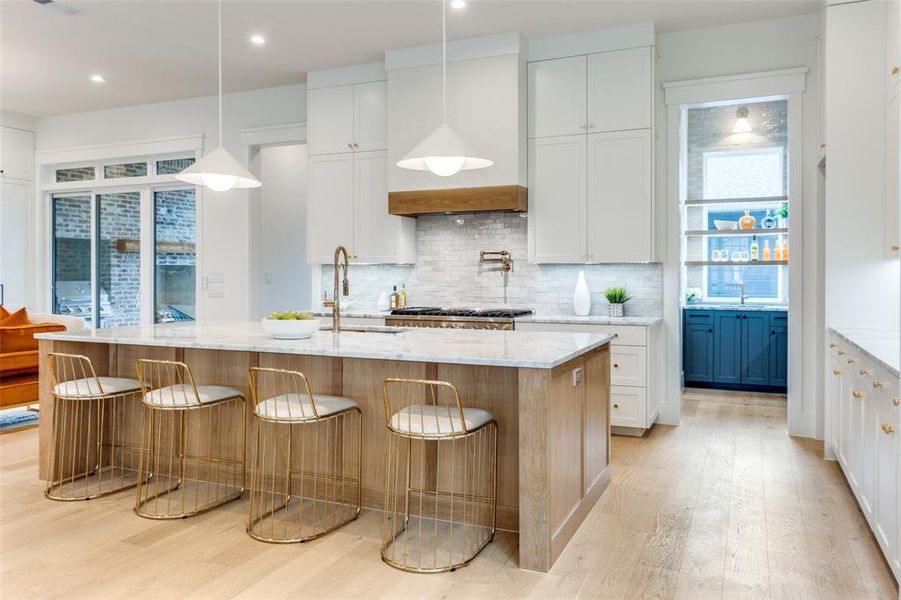 Kitchen featuring a large island with sink, light stone countertops, and white cabinets