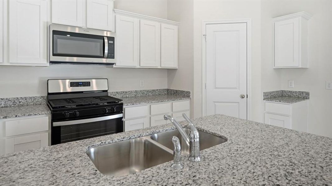 Kitchen featuring appliances with stainless steel finishes, white cabinetry, and light stone countertops Kitchen featuring appliances with stainless steel finishes, white cabinetry, and light stone countertops