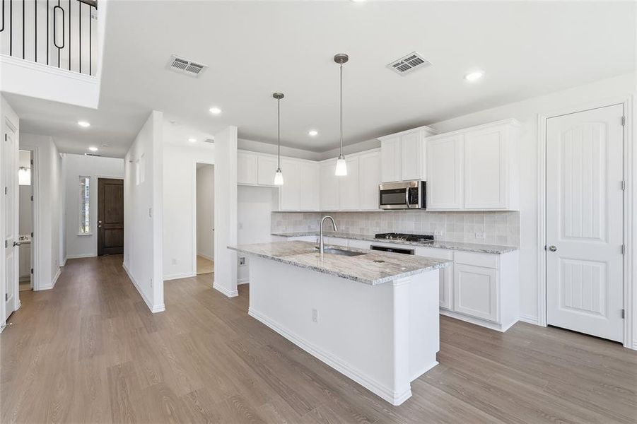 Kitchen with white cabinets, hanging light fixtures, light stone countertops, an island with sink, and stainless steel microwave