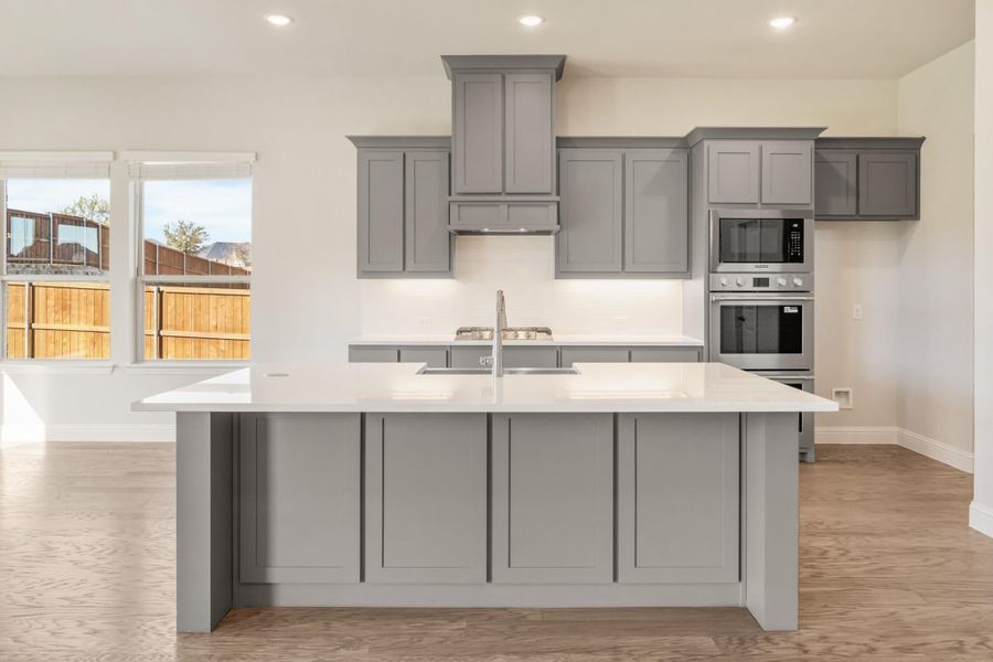 Kitchen with gray shaker cabinets, large island with white countertop, and stainless steel double oven Kitchen with gray shaker cabinets, large island with white countertop, and stainless steel double oven