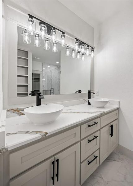 Full bath featuring a marble finish shower, light marble finish flooring, and double vanity