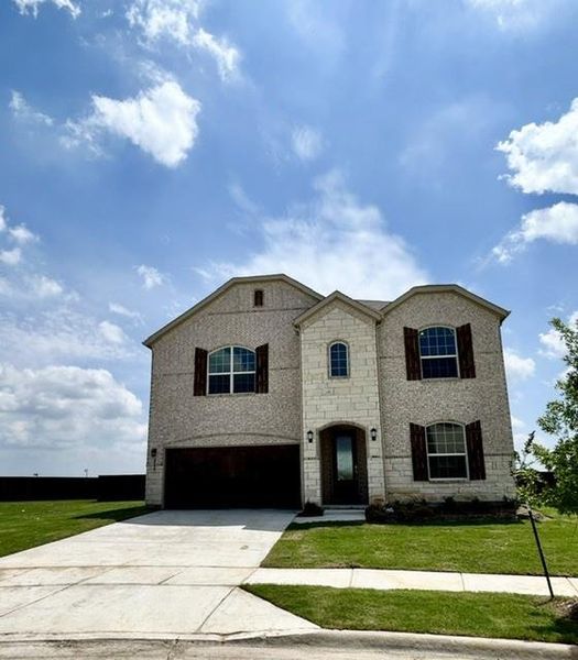 Two-story residence featuring a brick and stone facade, arched entryway, dark wood-finish garage door, and decorative window shutters Two-story residence featuring a brick and stone facade, arched entryway, dark wood-finish garage door, and decorative window shutters