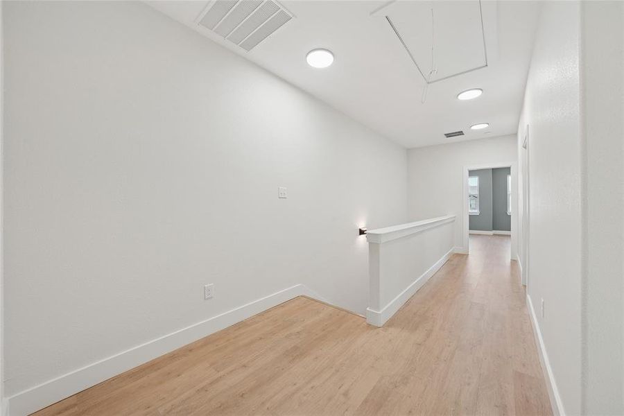 Corridor with an upstairs landing, attic access, light wood-style floors, and recessed lighting