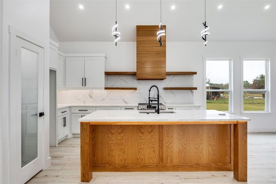 Kitchen with open shelves, light stone countertops, light wood-type flooring, and recessed lighting Kitchen with open shelves, light stone countertops, light wood-type flooring, and recessed lighting