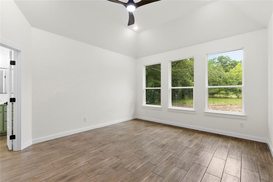 Spacious room featuring vaulted ceilings, recessed lighting, a modern ceiling fan, wood-finish flooring, and three large windows