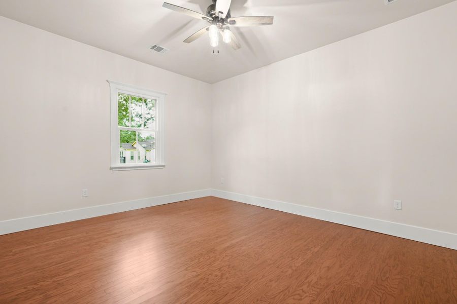 A well-lit bedroom features rich wood flooring and a refreshing ceiling fan for comfort. A well-lit bedroom features rich wood flooring and a refreshing ceiling fan for comfort.