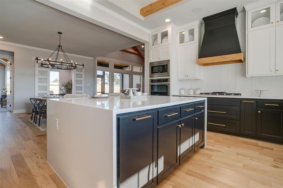 Kitchen with premium range hood, stainless steel appliances, beam ceiling, white cabinets, and a center island