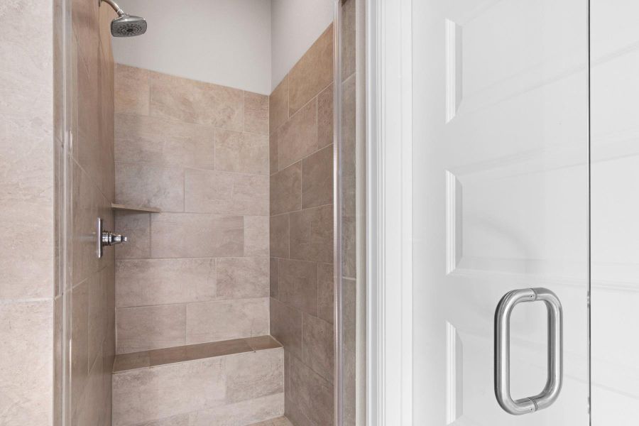 This photo showcases a modern shower with beige tile walls, a built-in bench, and a sleek glass door.