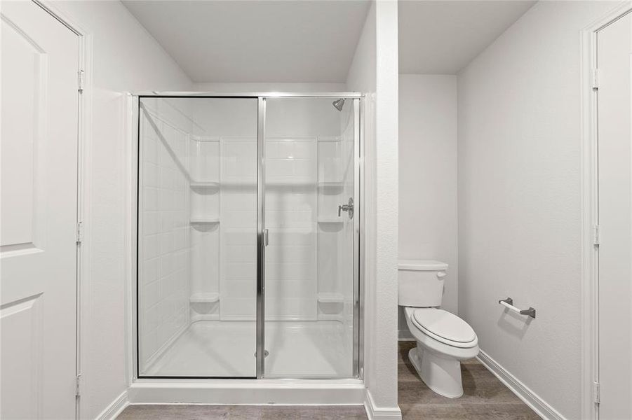 Bathroom featuring a shower with door, toilet, and hardwood / wood-style flooring