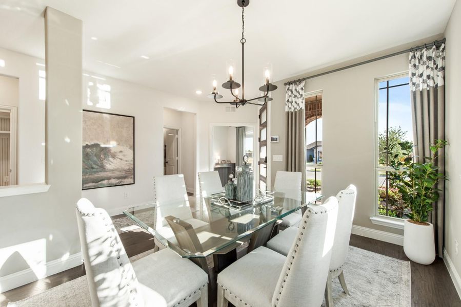 Dining room with glass table, six white upholstered chairs, chandelier, and large windows with curtains