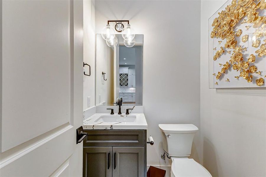 This modern powder room features a sleek vanity with a Calacatta Vega quartz top and oil-rubbed bronze fixtures. It also includes stylish gold floral wall art. The neutral tones create a clean and inviting space.