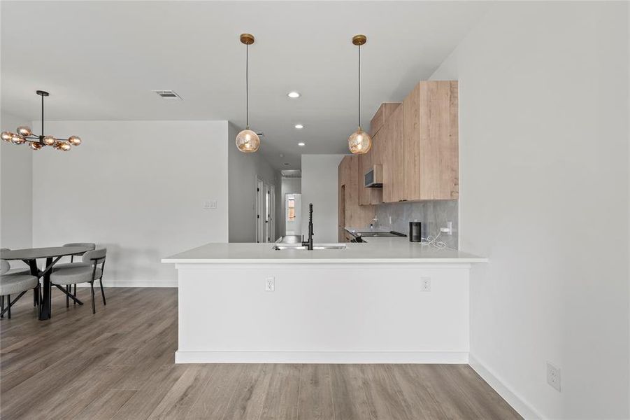 Kitchen featuring pendant lighting, backsplash, kitchen peninsula, sink, and wood-type flooring