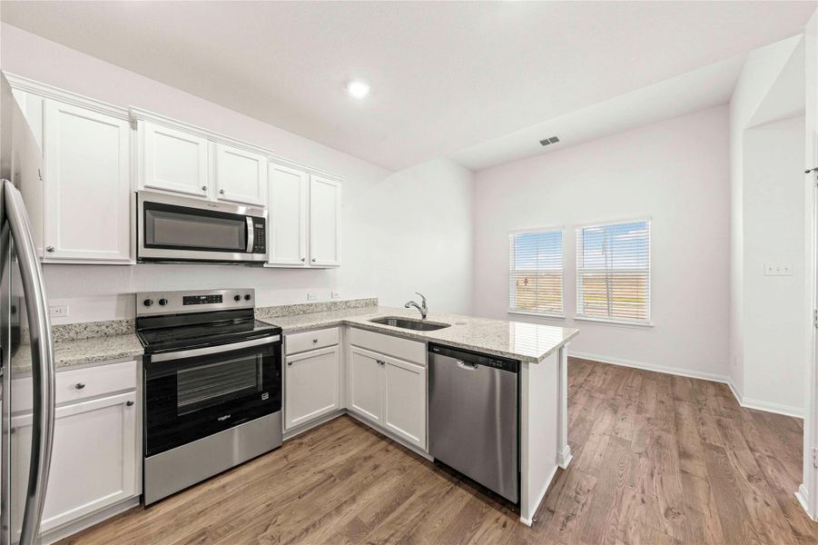 Kitchen with stainless steel appliances, white cabinetry, a peninsula, light wood-style floors, and recessed lighting Kitchen with stainless steel appliances, white cabinetry, a peninsula, light wood-style floors, and recessed lighting