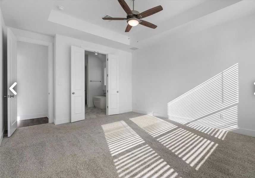 Unfurnished bedroom featuring ensuite bathroom, light carpet, ceiling fan, and a tray ceiling
