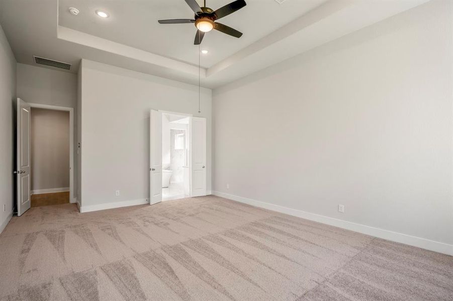 The primary bedroom with elegant tray ceiling and soft stain resistant carpet underfoot, inviting you to relax in style.