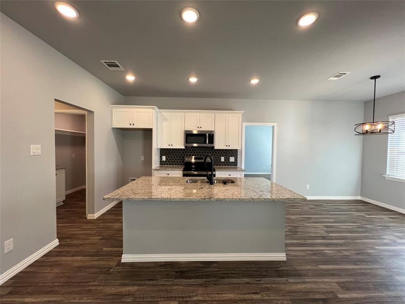 Kitchen with dark hardwood / wood-style flooring, stainless steel appliances, sink, white cabinets, and an island with sink