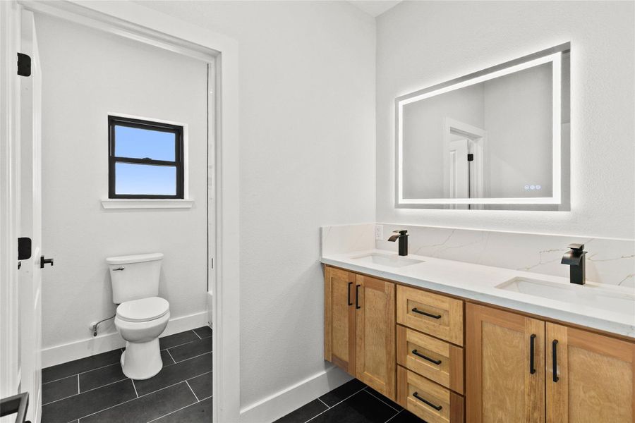 Thoughtfully designed guest bathroom featuring a floating double vanity, illuminated mirror, and a separate tub/shower and water closet area for added comfort and convenience.