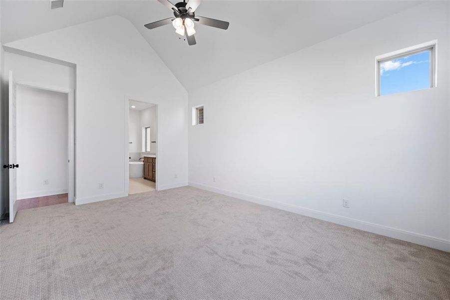 Unfurnished bedroom with light colored carpet, high vaulted ceiling, ensuite bath, and ceiling fan