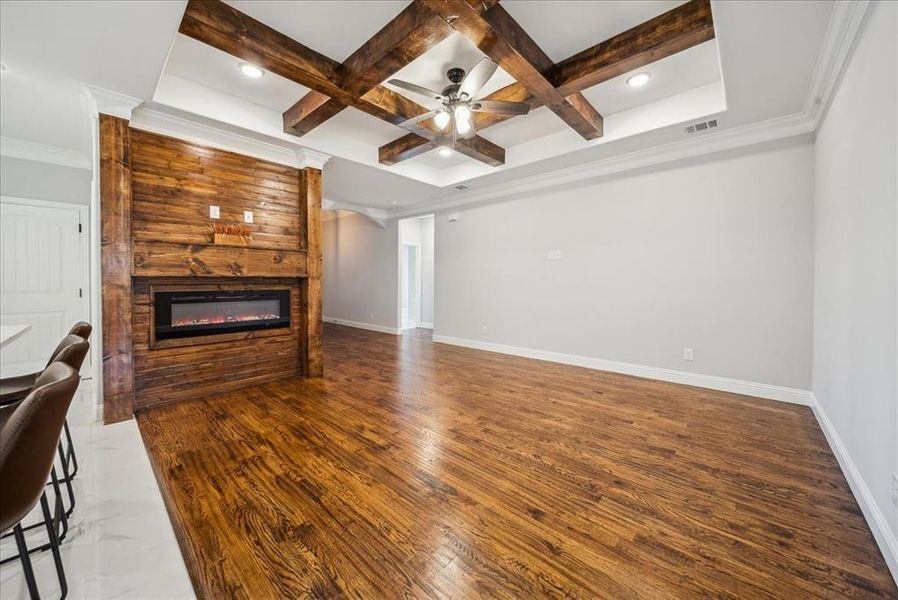 Unfurnished living room with beamed ceiling, a large fireplace, ornamental molding, ceiling fan, and coffered ceiling