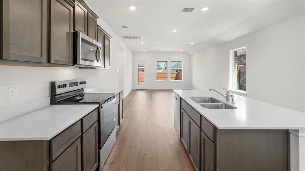 Kitchen featuring stainless steel appliances, dark wood-finish cabinetry, white countertops, and wood-finish flooring