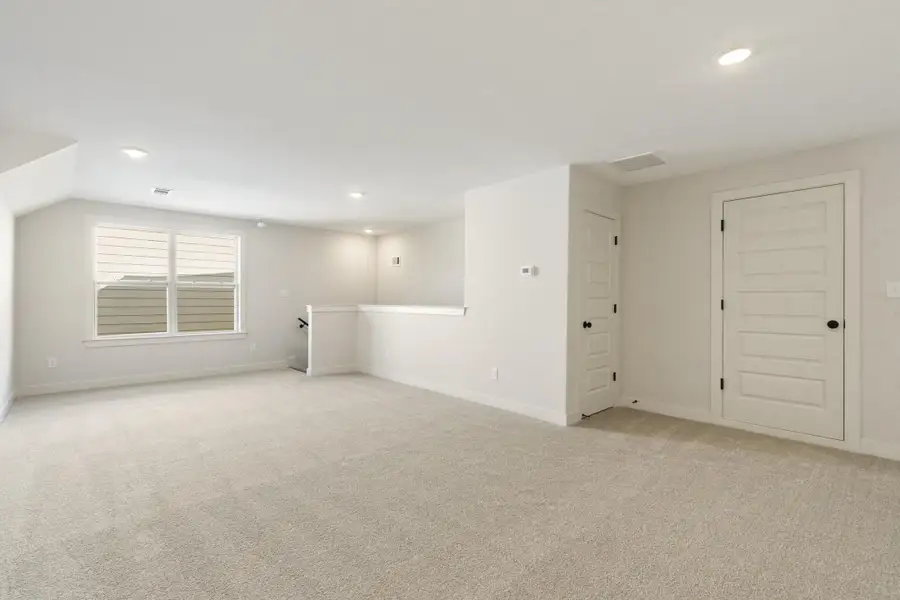 Carpeted open-concept space featuring recessed lighting, a window, a partial wall, and multiple doors Carpeted open-concept space featuring recessed lighting, a window, a partial wall, and multiple doors