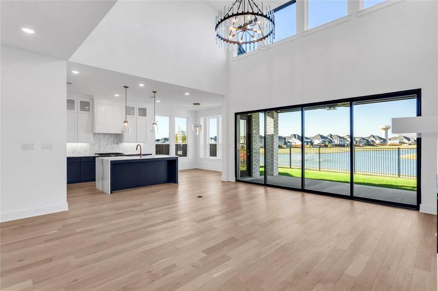 Unfurnished living room featuring a residential view, light wood finished floors, recessed lighting, a chandelier, and a high ceiling