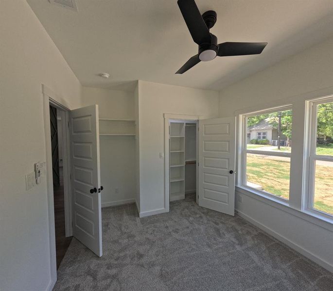 Unfurnished bedroom with dark colored carpet, a walk in closet, and a ceiling fan Unfurnished bedroom with dark colored carpet, a walk in closet, and a ceiling fan