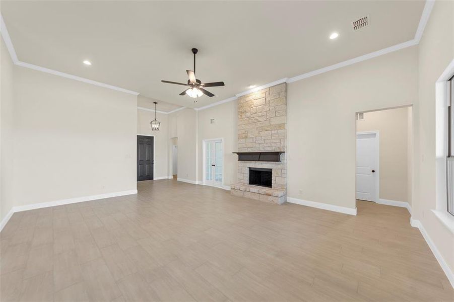 Unfurnished living room with ceiling fan, a stone fireplace, light wood-type flooring, crown molding, and recessed lighting Unfurnished living room with ceiling fan, a stone fireplace, light wood-type flooring, crown molding, and recessed lighting
