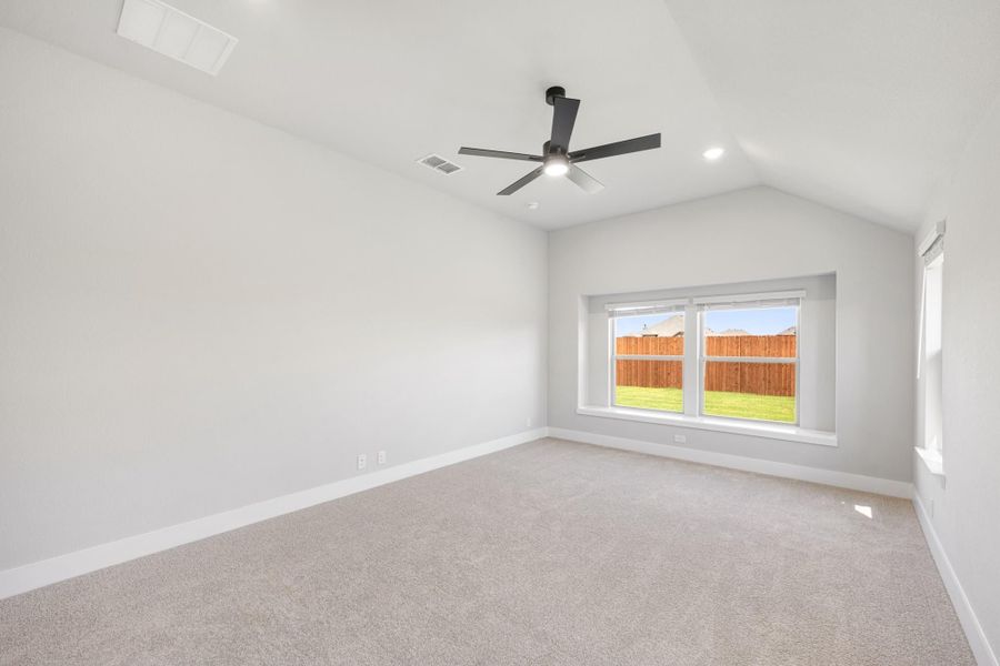 Empty bedroom with vaulted ceiling, ceiling fan, carpet flooring, and backyard window view Empty bedroom with vaulted ceiling, ceiling fan, carpet flooring, and backyard window view