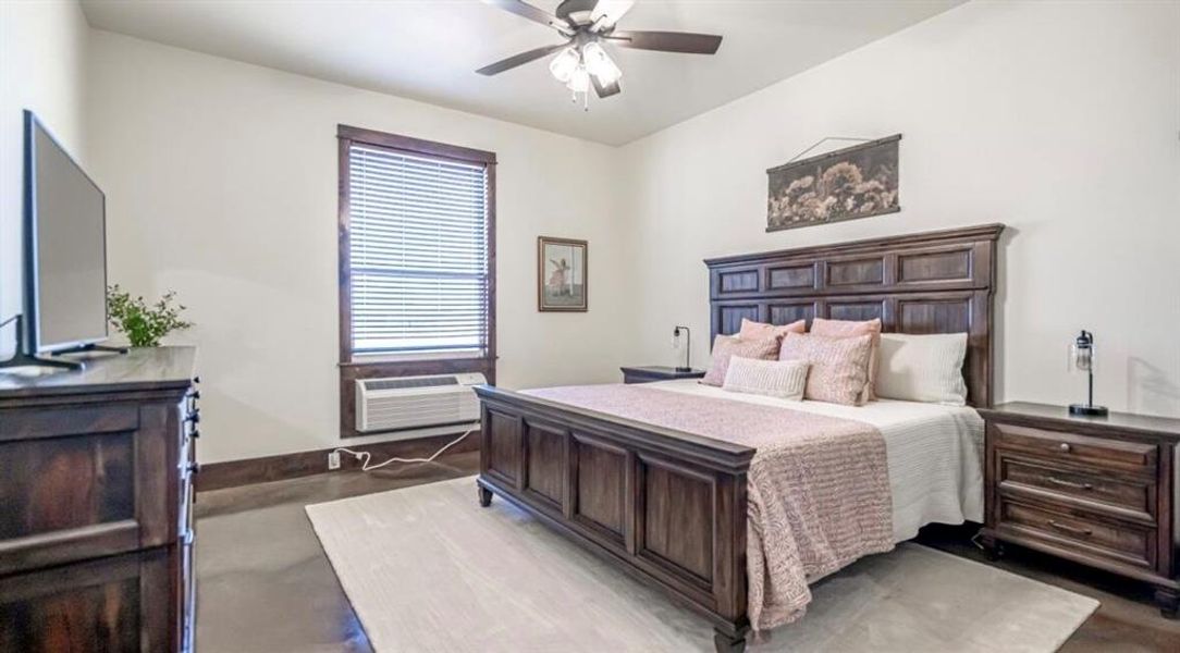 Bedroom featuring baseboards, finished concrete flooring, ceiling fan, and an AC wall unit Bedroom featuring baseboards, finished concrete flooring, ceiling fan, and an AC wall unit