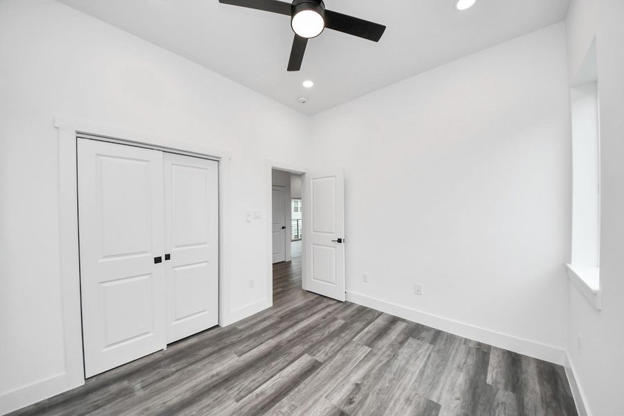 Bright, modern room with sleek vinyl flooring, white walls, and a ceiling fan. Includes a double-door closet and a window for natural light. Bright, modern room with sleek vinyl flooring, white walls, and a ceiling fan. Includes a double-door closet and a window for natural light.