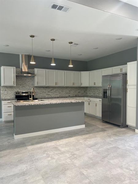 Kitchen with stainless steel appliances, decorative backsplash, wall chimney range hood, an island with sink, and pendant lighting. Kitchen with stainless steel appliances, decorative backsplash, wall chimney range hood, an island with sink, and pendant lighting.
