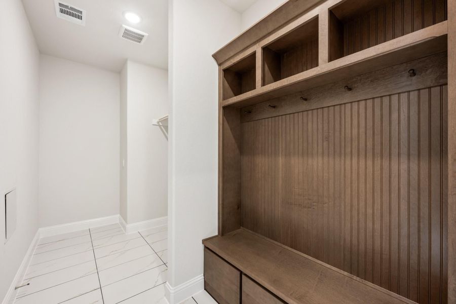 Mudroom with built-in wood locker unit featuring upper cubbies, coat hooks, bench, and drawer storage on white tile floor Mudroom with built-in wood locker unit featuring upper cubbies, coat hooks, bench, and drawer storage on white tile floor