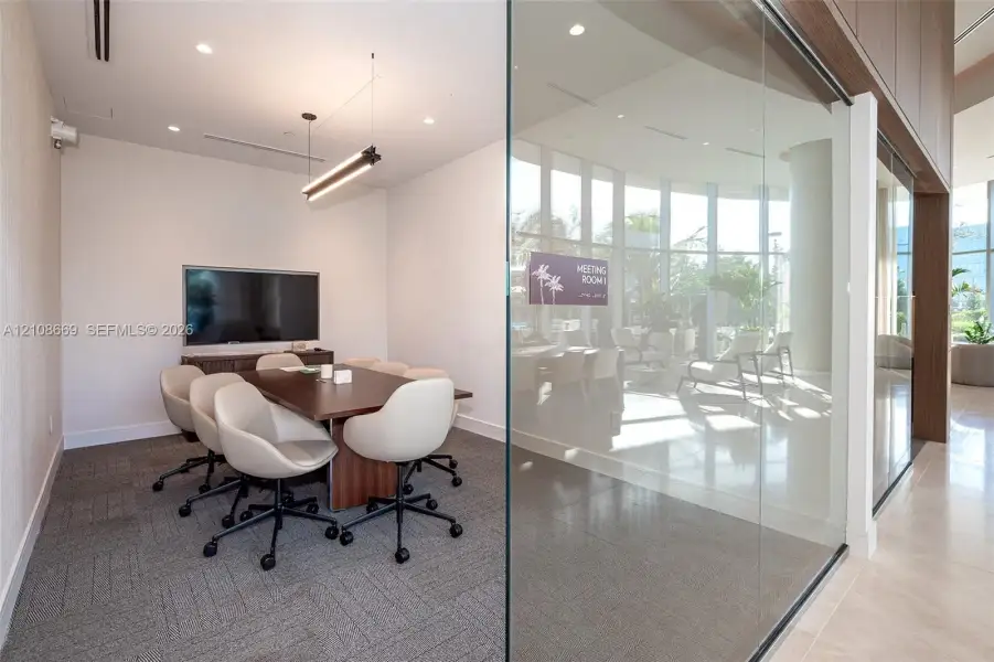 Glass-enclosed workspace featuring floor-to-ceiling glazing, linear pendant lighting, neutral carpeting, and a built-in display screen