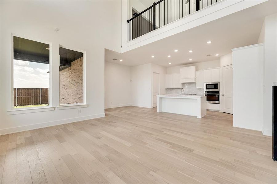 Unfurnished living room with light wood-style flooring, a towering ceiling, and recessed lighting Unfurnished living room with light wood-style flooring, a towering ceiling, and recessed lighting