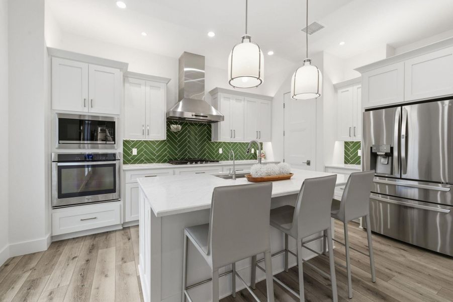 Kitchen with stainless steel appliances, a center island with sink, white cabinets, a kitchen bar, and light wood-type flooring
