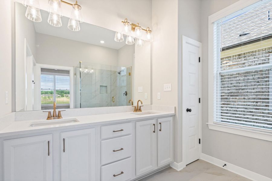 Bathroom featuring a dual vanity with white cabinetry, light-toned countertops, and gold-finish fixtures