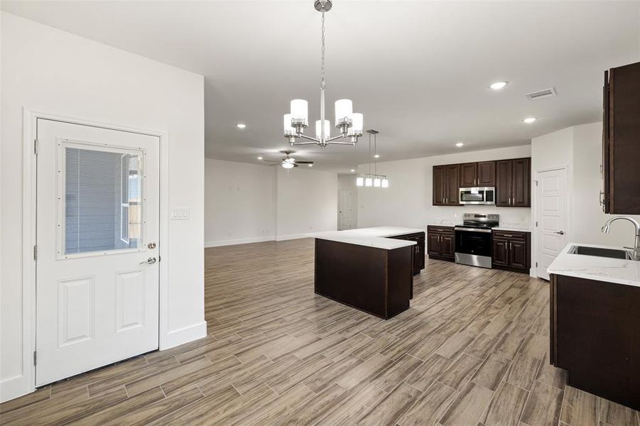 Kitchen with hanging light fixtures, sink, appliances with stainless steel finishes, a center island, and light hardwood / wood-style floors