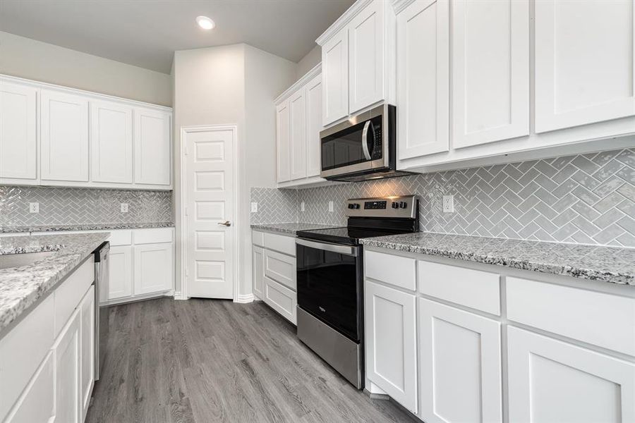 Kitchen with white cabinetry, light stone counters, appliances with stainless steel finishes, light hardwood / wood-style flooring, and backsplash