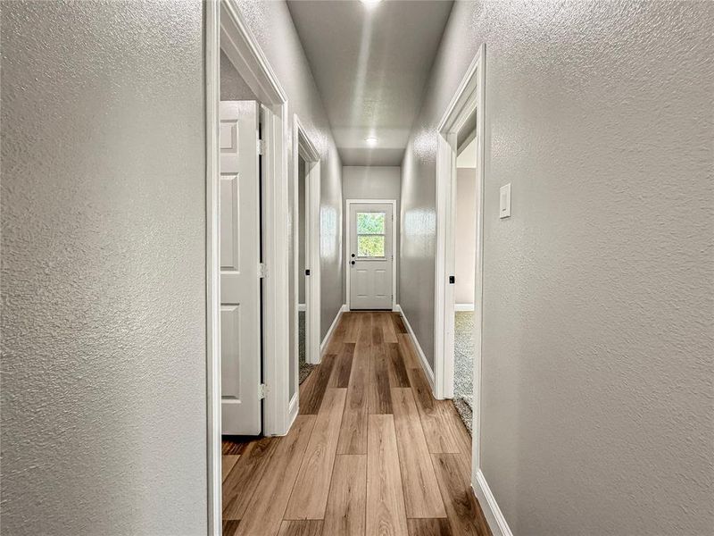 Hallway featuring wood-finish flooring, light gray walls, white trim, recessed lighting, and panel doors Hallway featuring wood-finish flooring, light gray walls, white trim, recessed lighting, and panel doors