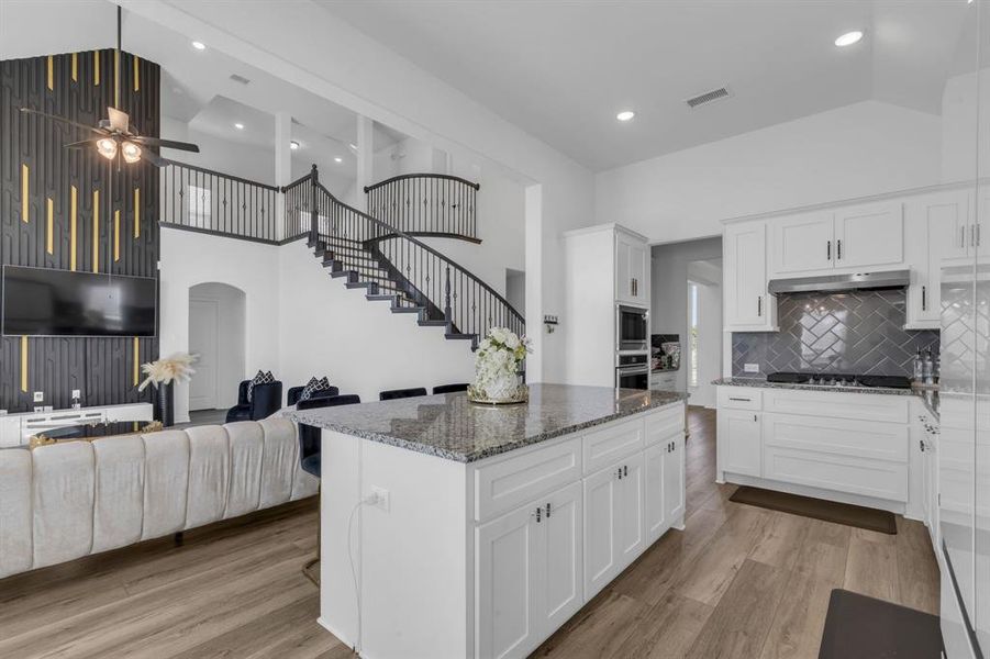 Kitchen with high vaulted ceiling, white cabinetry, light hardwood / wood-style floors, and decorative backsplash