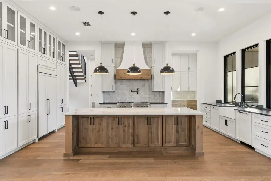 Dual tone kitchen with a large island, paneled built in fridge, dark stone countertops, light wood-style floors, and two tone cabinets