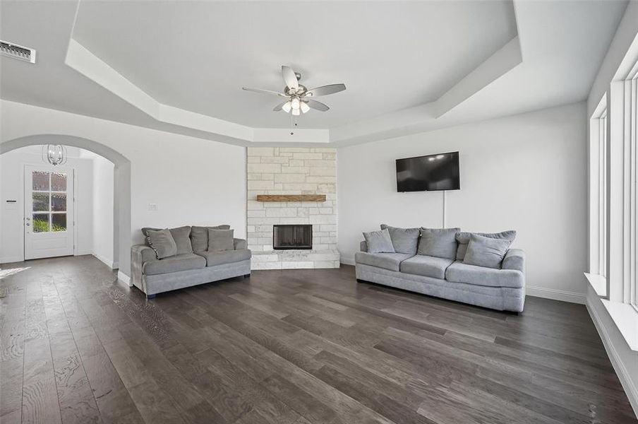 Living room featuring a raised ceiling, dark wood-style floors, and a ceiling fan