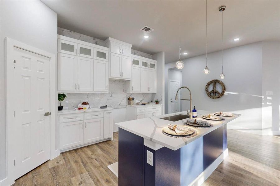 Kitchen featuring pendant lighting, sink, backsplash, an island with sink, and white cabinets